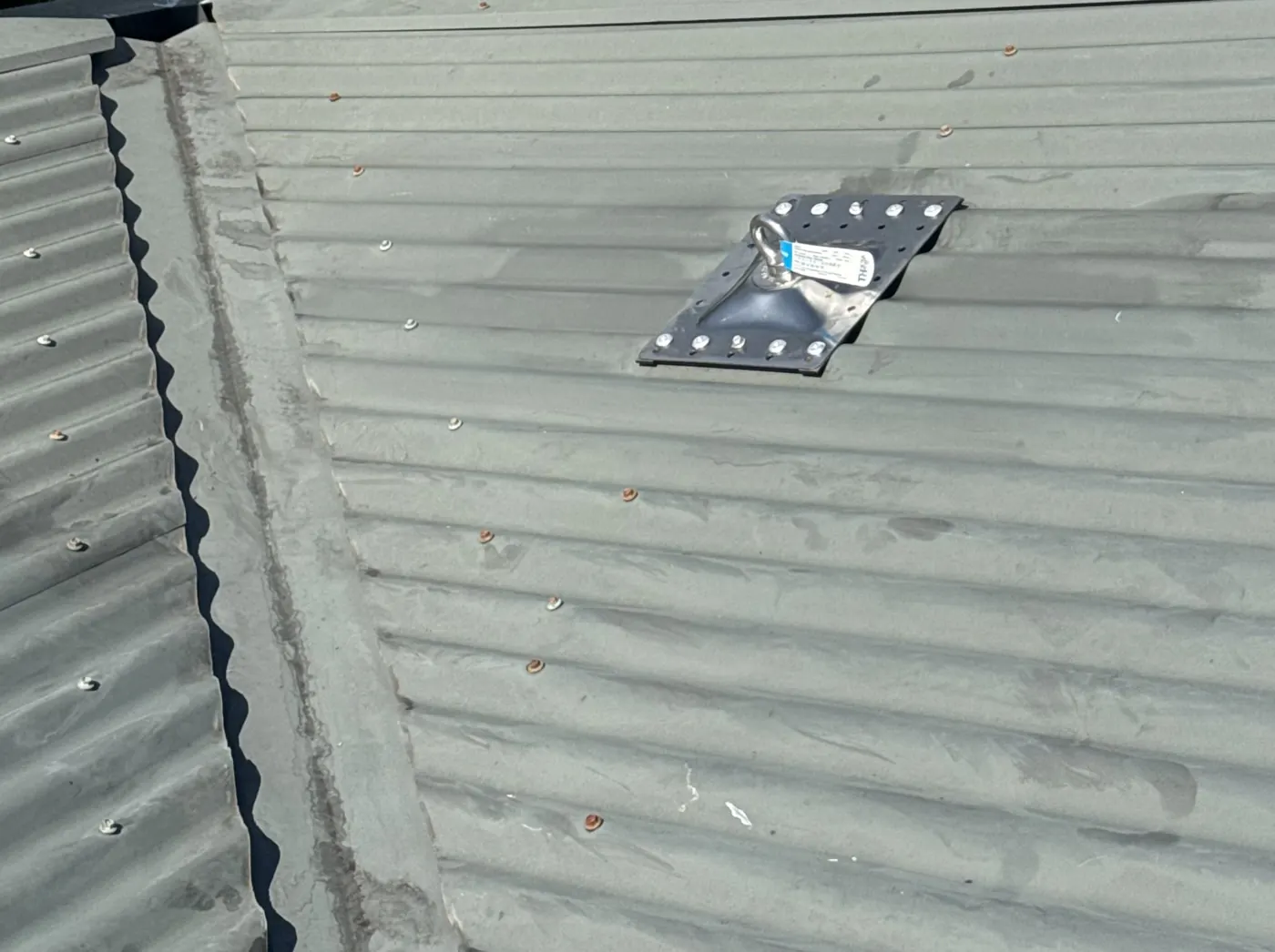 Roof anchor plate fixed to a corrugated metal roof near the edge