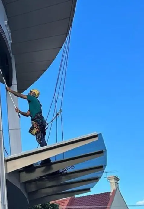 Commercial window cleaning on rope above a curved glass entrance canopy