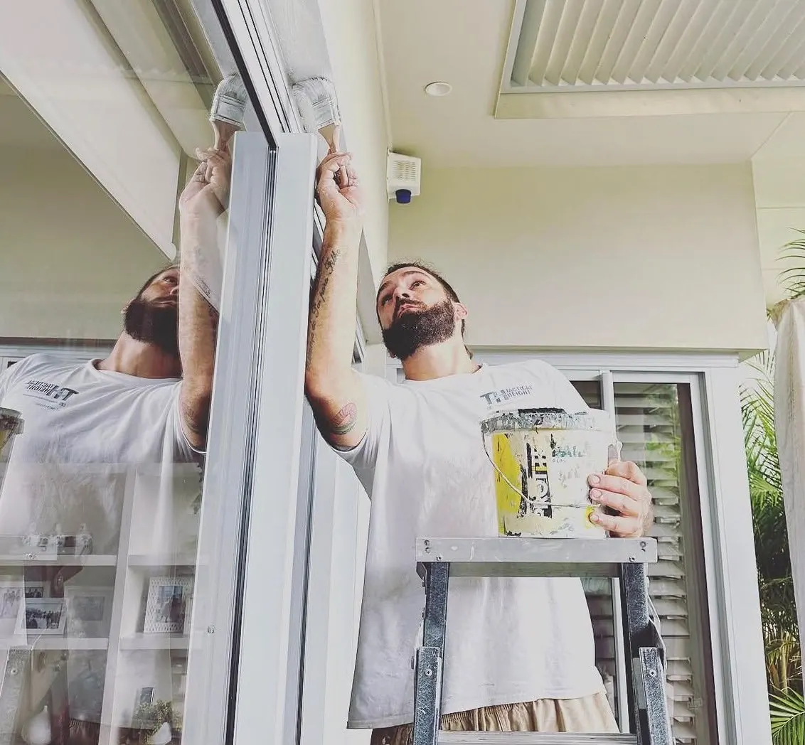 Painter on a ladder cutting in a window frame during a house repaint