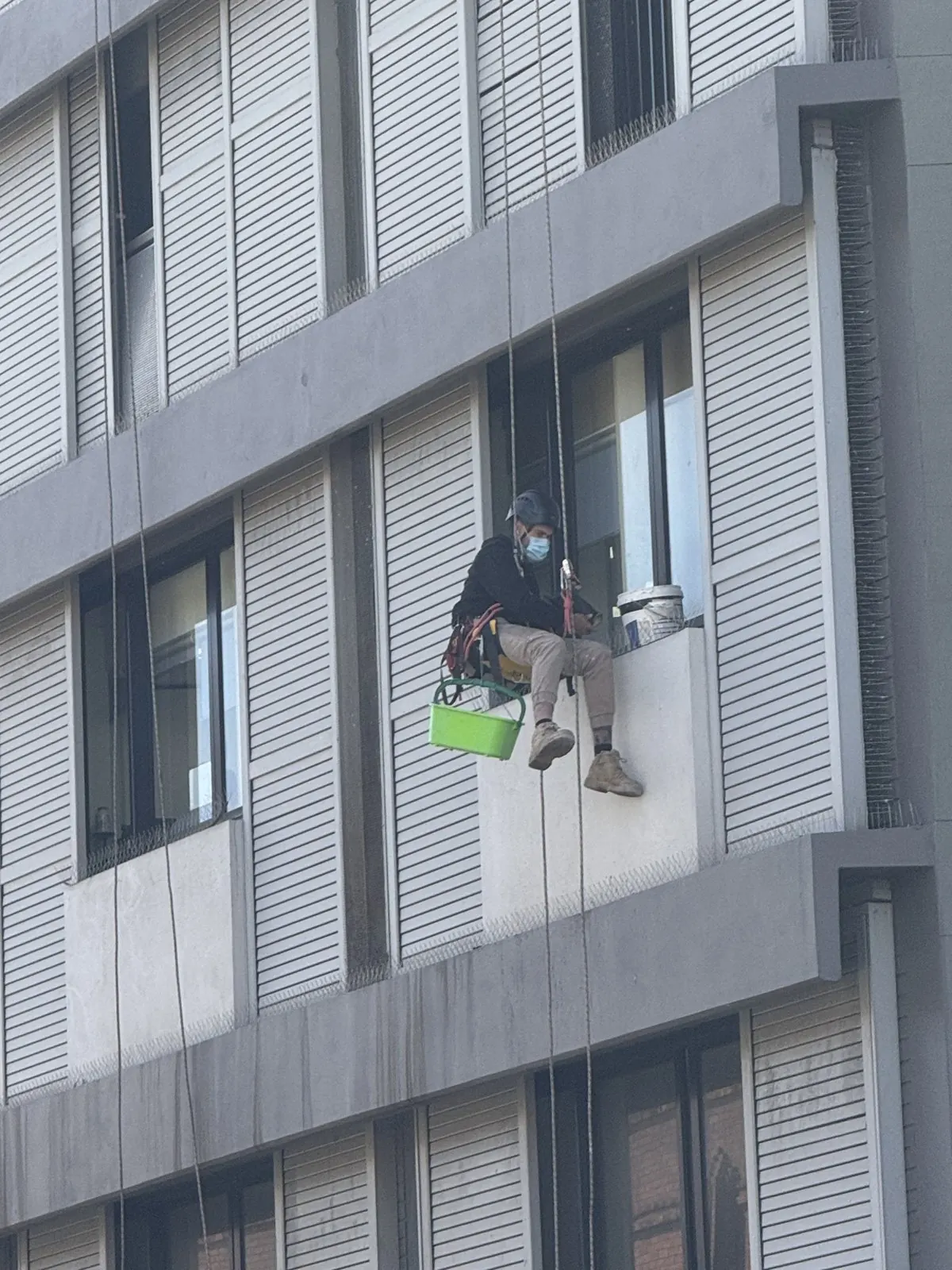 Technician on rope cleaning a window ledge on a grey façade with louvres