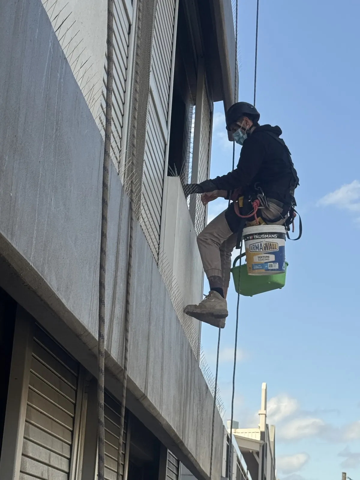 Technician on rope with buckets cleaning a high ledge