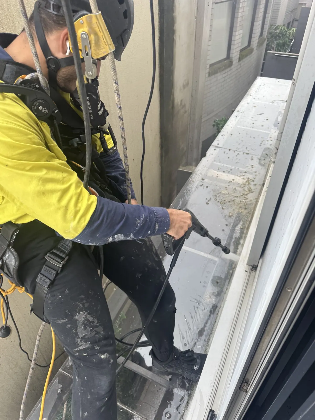Pressure cleaning a window ledge from the rope, technician in hi-vis