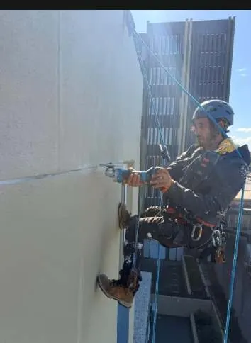 Technician on rope cutting a new movement joint into a rendered wall in Mascot