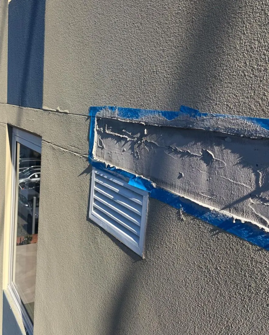 Render repair built up around a wall vent on the Mascot façade