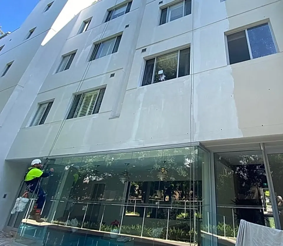 Technician on rope coating a white rendered façade above a shopfront