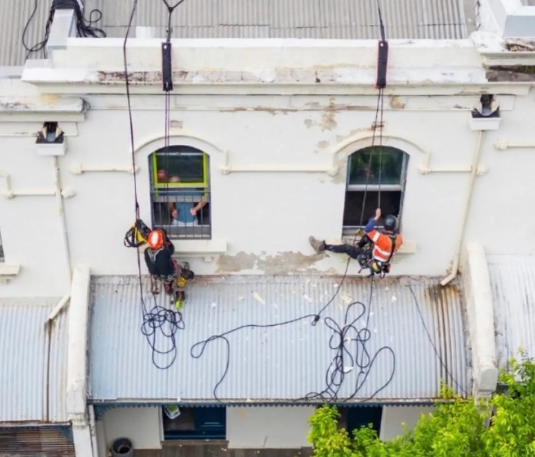 Two technicians on rope repairing the heritage façade above the street awning in Redfern