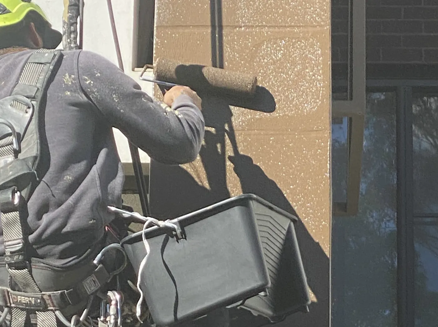 Painter on rope rolling paint onto a rendered wall