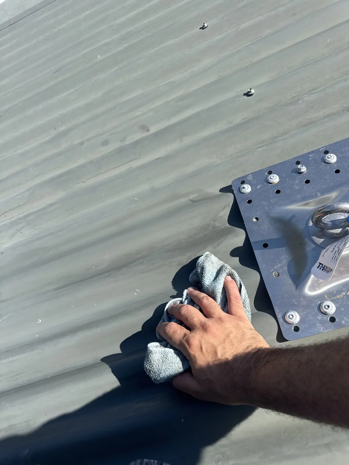 Hand cleaning around a new roof anchor plate on a metal roof