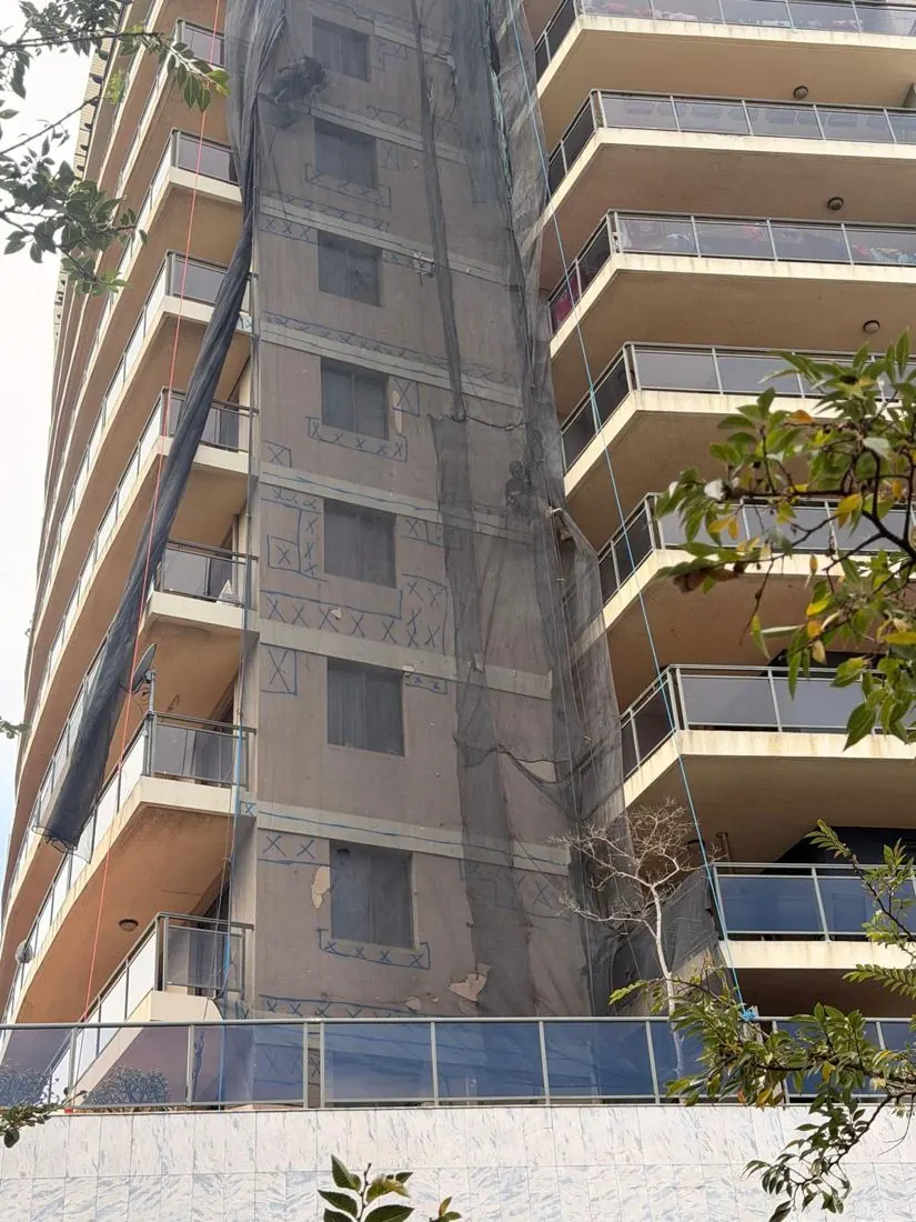 Containment netting on a strata tower during façade repairs, protecting balconies and the footpath